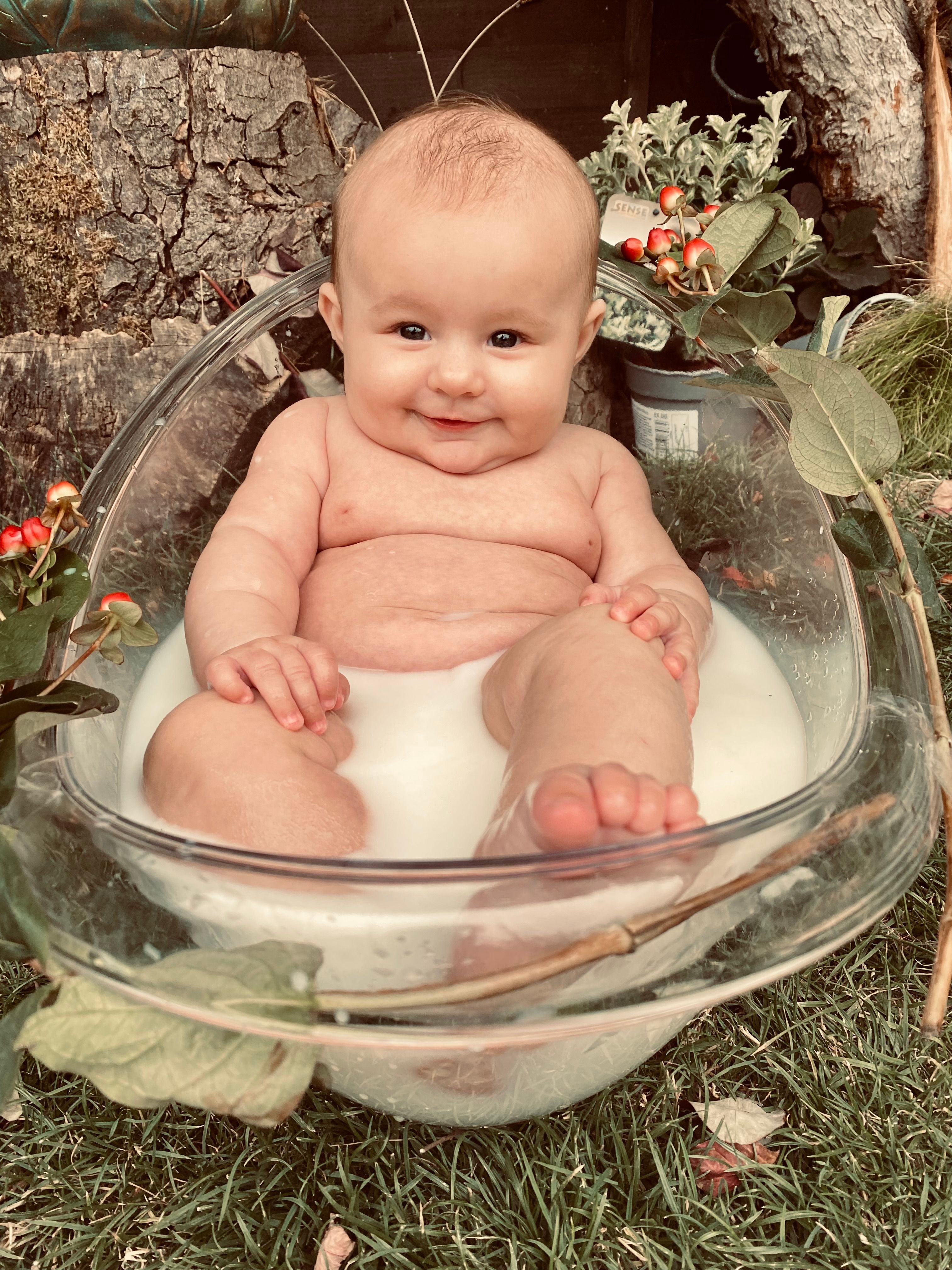 Adorable baby enjoying a milk bath surrounded by nature, with a joyful smile, captured outdoors.