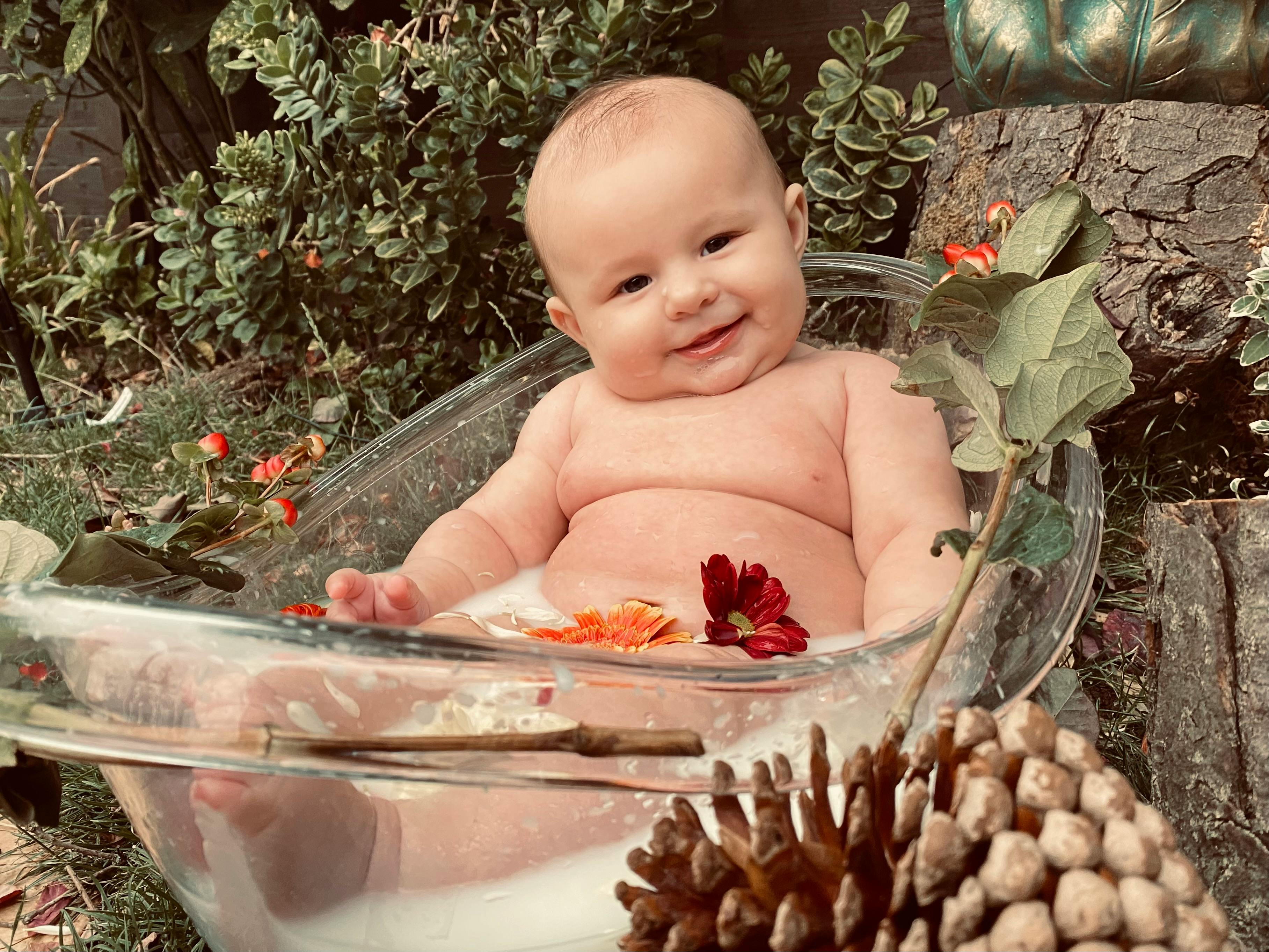 Charming baby enjoying an outdoor bath surrounded by flowers, smiling warmly.