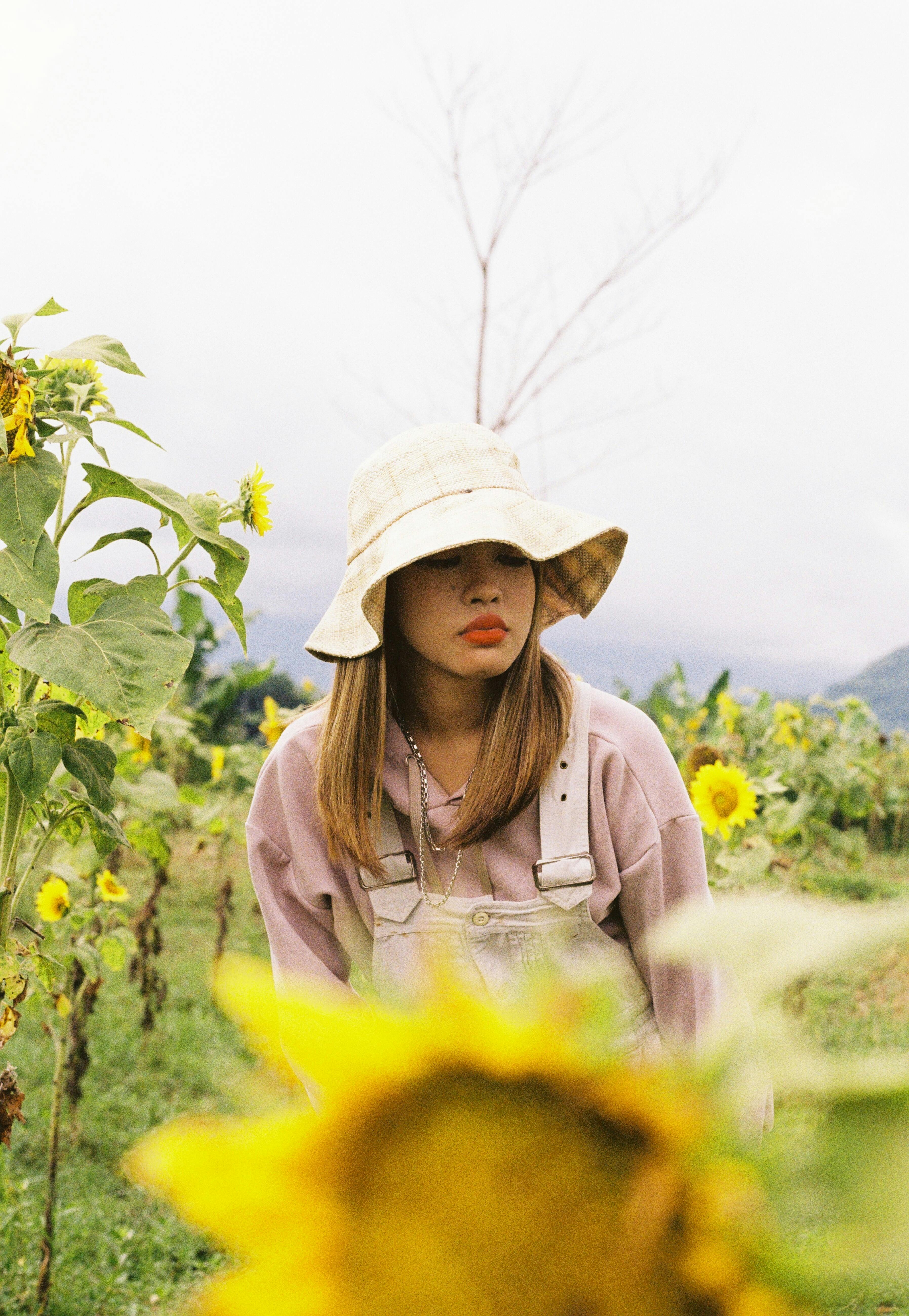 Portrait of a woman in a pink sweater and bucket hat amidst a vibrant sunflower field.