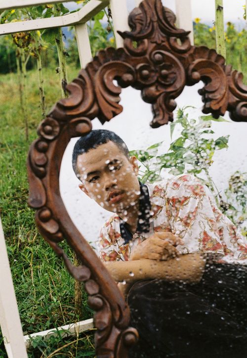Free Asian man in floral shirt reflected in a rain-speckled mirror outdoors. Stock Photo