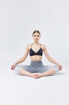 Yoga instructor in a black top performs a seated yoga pose in a studio setting.