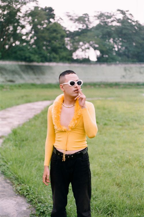 Free Stylish young adult in yellow top and sunglasses smoking outdoors on a grassy field. Stock Photo