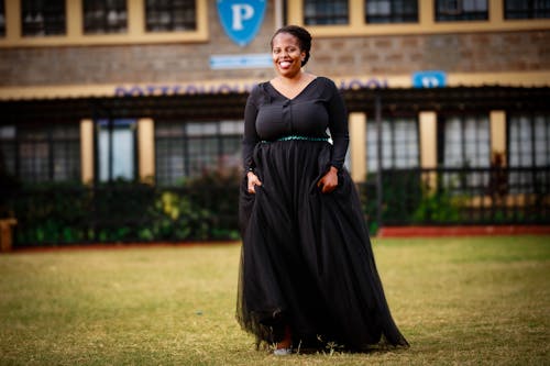 A Woman in Black Dress Standing on Green Grass Field