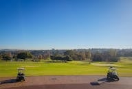 晴朗的日子里，蔚蓝的天空下，高尔夫球场全景中停着高尔夫球车