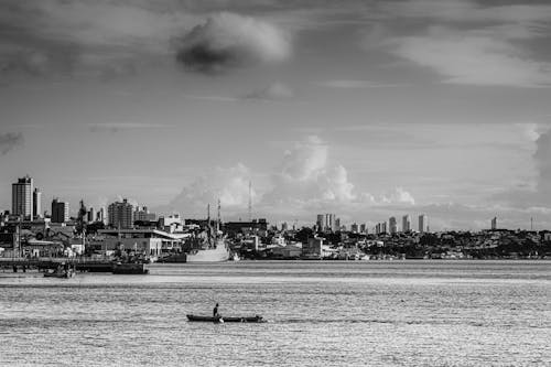A Grayscale Photo of a Sailing Boat on the Sea Near the City Buildings