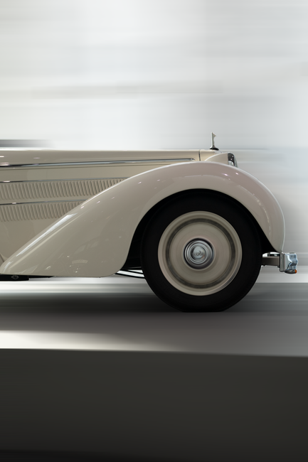 Side profile of a classic white vintage car in motion, showcasing elegant design.