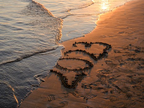 Romantic hearts drawn in the sand during a serene sunset on the beach.