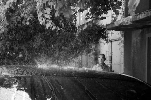 Black and white photo of a man staring during a rainy day with splashing raindrops.