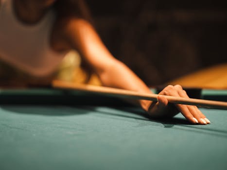 Focused close-up of a player's hand holding a billiards cue during a game. Perfect for sports or lifestyle themes.