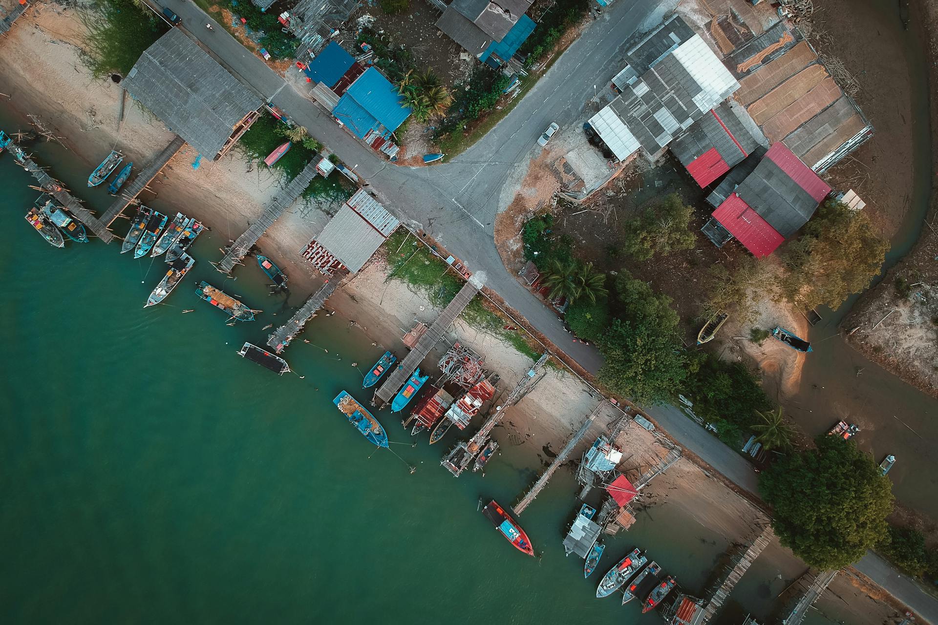 Drone shot capturing a quaint coastal fishing village with boats docked at jetties along the shoreline.