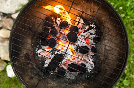 Top view of a charcoal grill with orange glowing embers and flames, ready for outdoor cooking.
