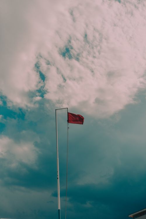 Free Red warning flag flying high near Igea Marina with an overcast sky. Stock Photo