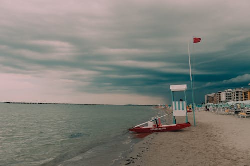 White and Red Boat on Seashore Under Gloomy Sky