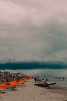 A moody beach scene in Igea Marina, Italy, featuring dramatic clouds and empty loungers.