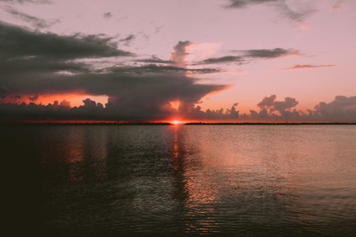 Free Captivating sunset over the ocean with striking clouds and serene reflections. Stock Photo