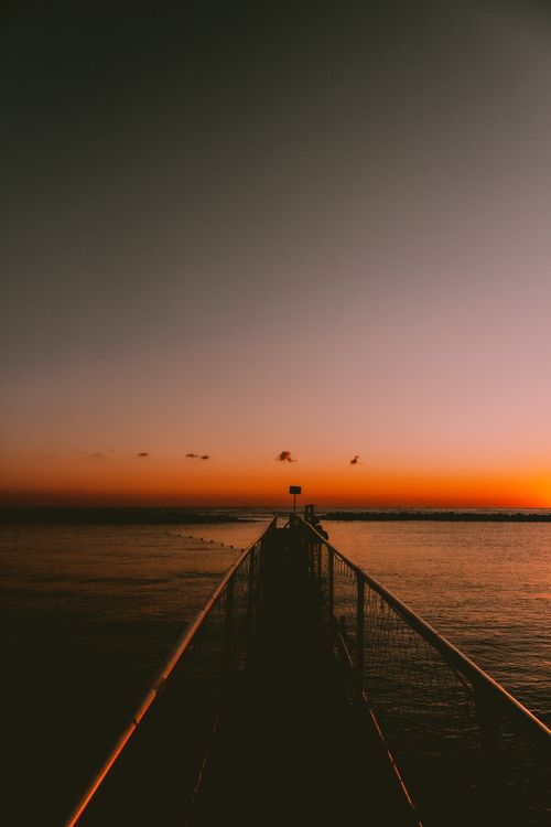 Free A tranquil scene of a pier at Igea Marina during a vibrant sunset, capturing serene beauty. Stock Photo