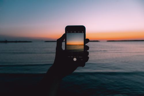 Free Hand holding smartphone capturing sunset by the ocean at Igea Marina, Italy. Stock Photo