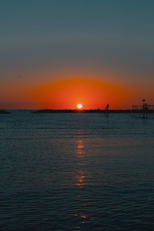 Free Vibrant sunset over the calm waters of Igea Marina, Italy, casting a silhouette on the horizon. Stock Photo