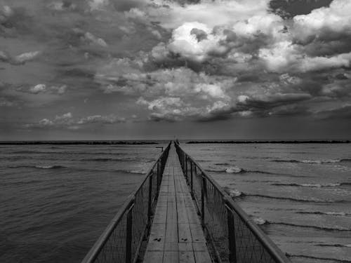 A Grayscale Photo of a Wooden Dock on the Sea Under the Cloudy Sky