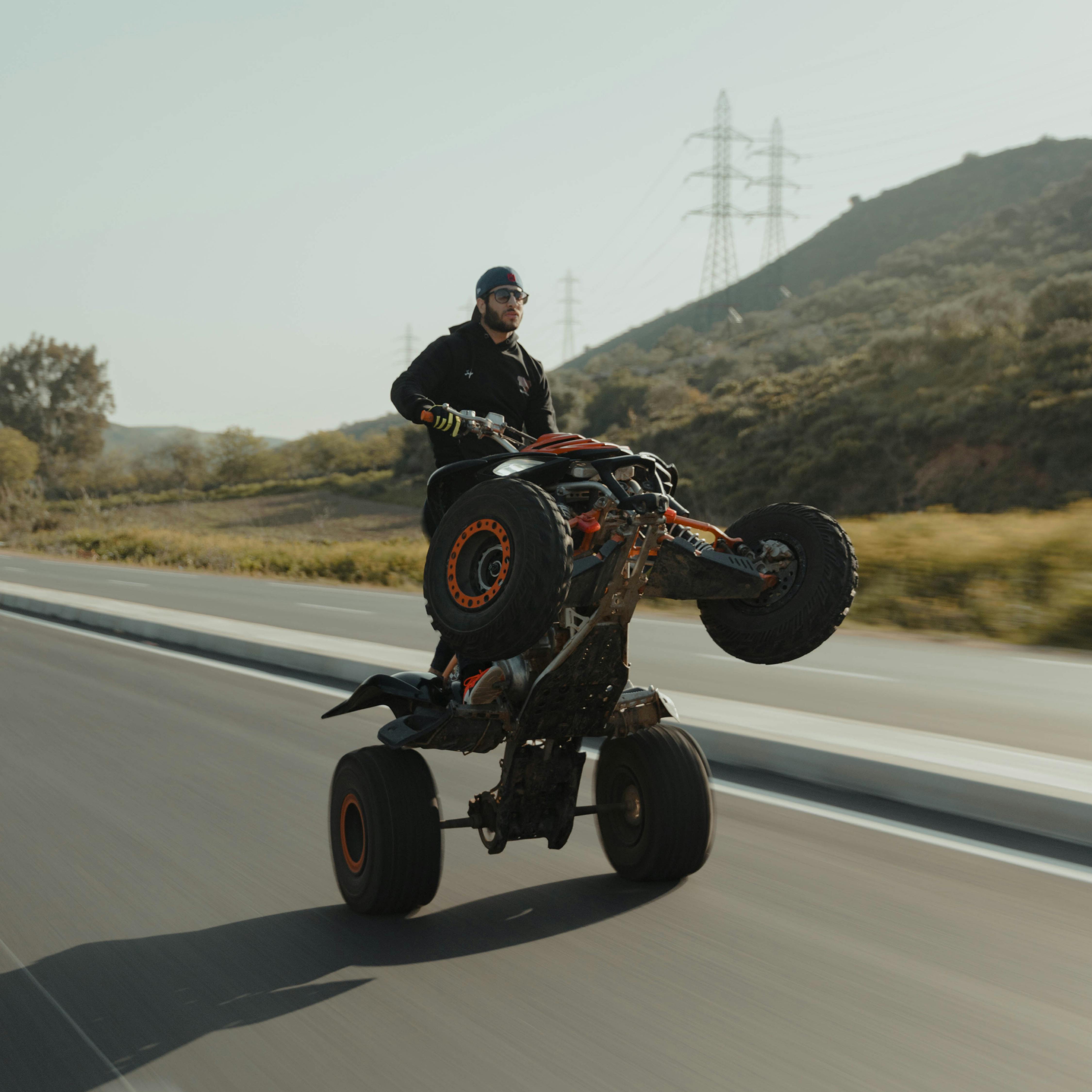 A man skillfully performs a wheelie on a quad bike on an open road.