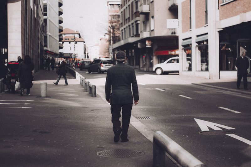 Man in black blazer strolls through a bustling Lugano street during the day.