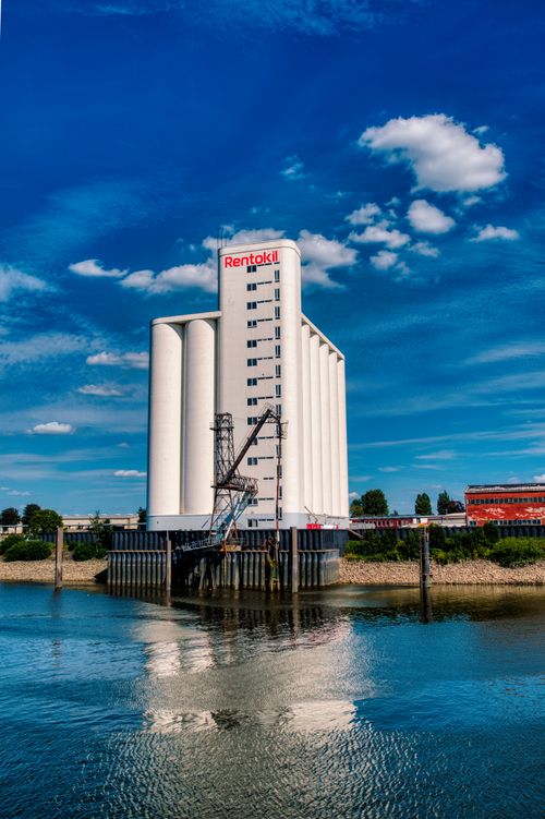 Free Tall white industrial building on waterfront with blue sky reflection. Stock Photo