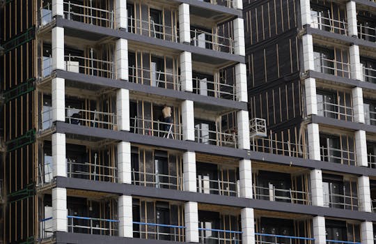 View of a modern high-rise building under construction, featuring scaffolding and workers.