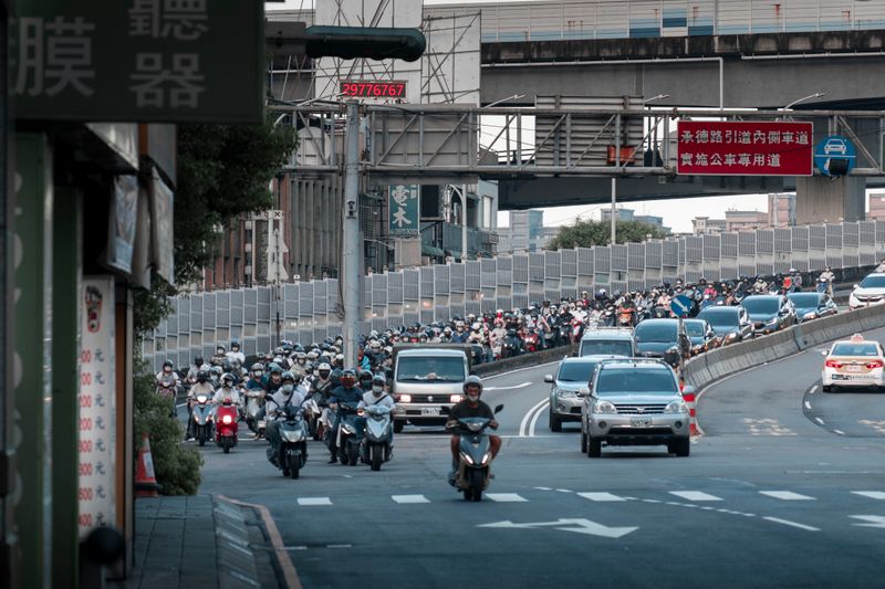 An urban street full of motorbikes and vehicles during the day in a bustling city.