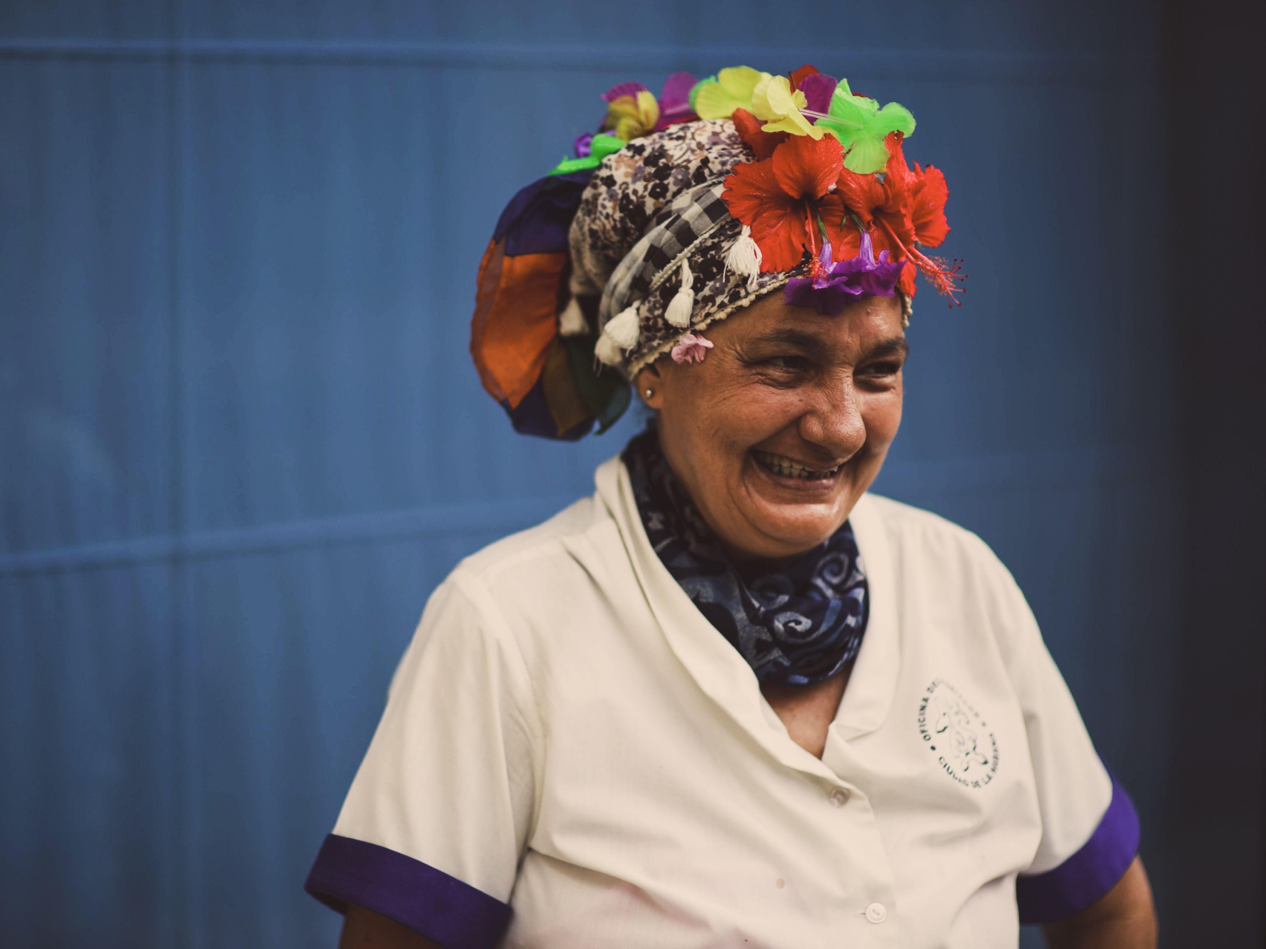 A smiling woman wearing a floral headdress stands against a blue background.