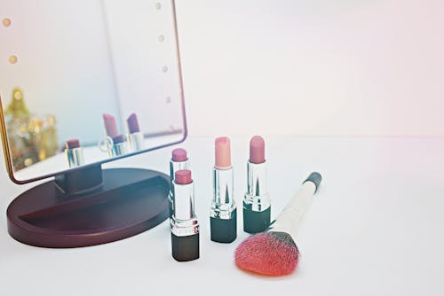 Four Assorted-color Lipsticks Beside Makeup Brush