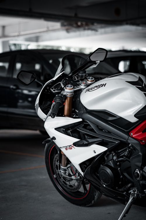 Free Close-up of a white Triumph Daytona 675 motorcycle parked indoors with cars in the background. Stock Photo