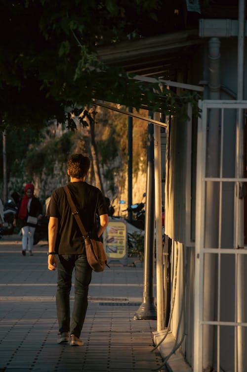 Back View of a Man with a Bag Walking on the Sidewalk