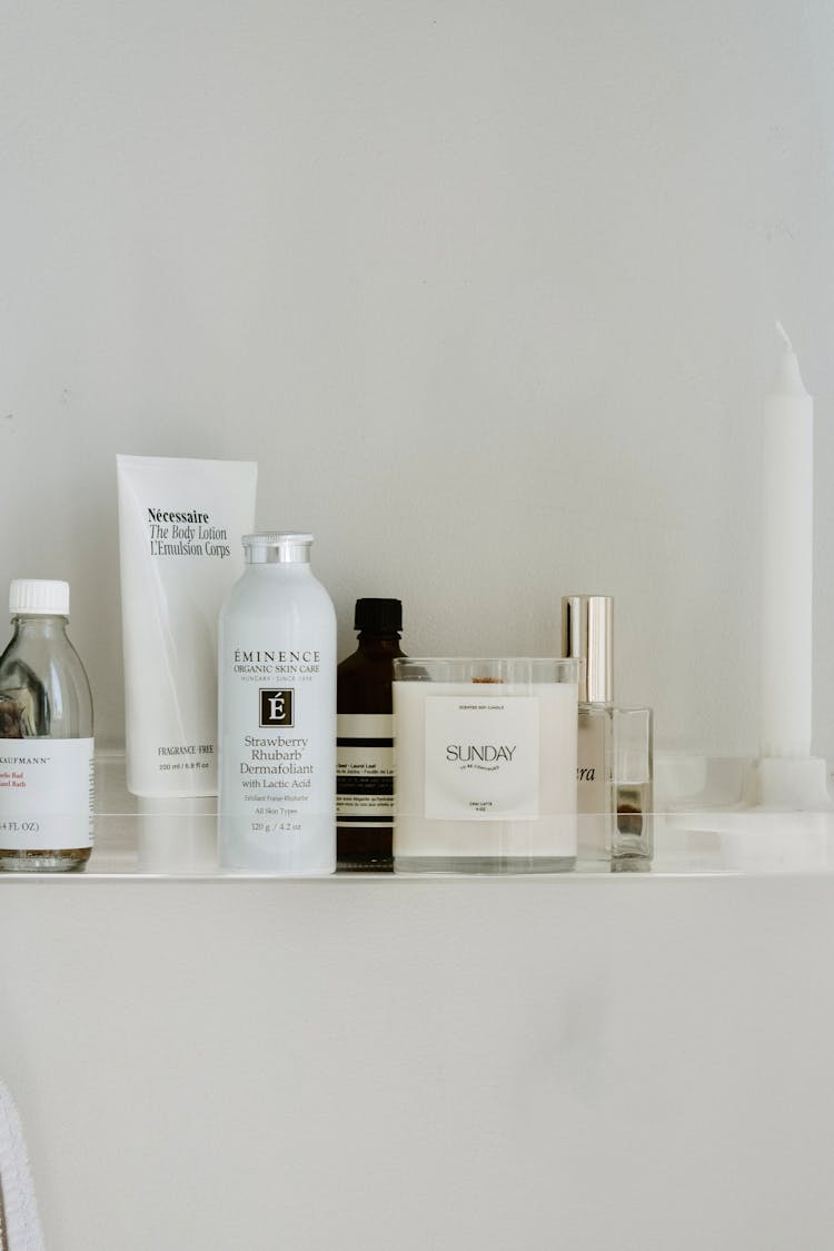 Branded Cosmetics And White Candle Standing On Shelf