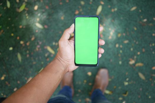 Close-up of a hand holding a smartphone with a green screen outdoors, ideal for mockups.
