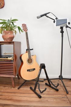 A cozy indoor setup featuring an acoustic guitar, microphone, and tablet. Perfect for music enthusiasts.
