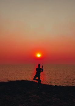 A tranquil silhouette of a person practicing yoga near the ocean during a stunning sunset.
