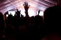 大帐篷下，灯光明亮，人群欢呼着举起双手，音乐会气氛充满活力