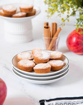 A tempting display of muffins dusted with sugar, surrounded by cinnamon sticks and apples.
