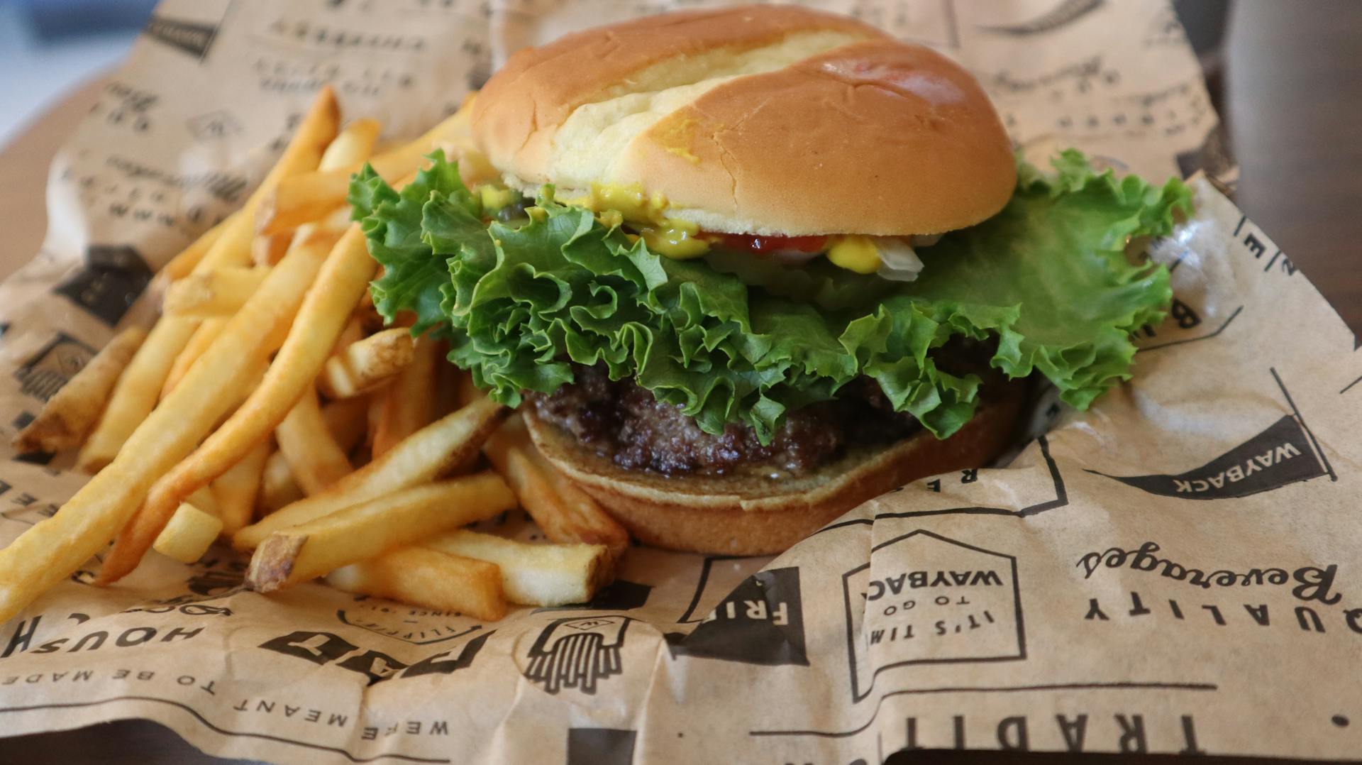 Tasty beef burger with French fries served on printed paper in Sacramento.