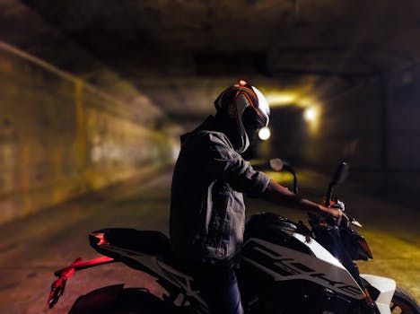 A motorbike rider pauses in an illuminated urban tunnel, capturing a dramatic nighttime scene.