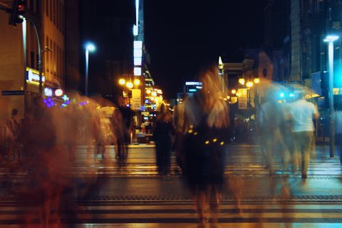 Free Blurred pedestrians crossing street at night with city lights. Stock Photo