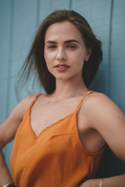 Portrait of a confident woman in an orange dress posing against a blue backdrop, exuding elegance and style.