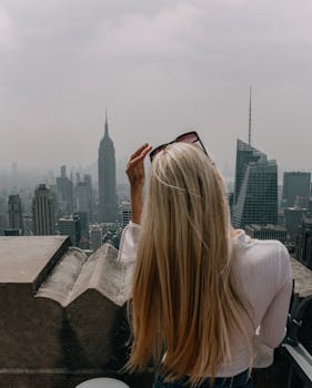 Blonde woman with sunglasses views New York City skyline, featuring the Empire State Building.