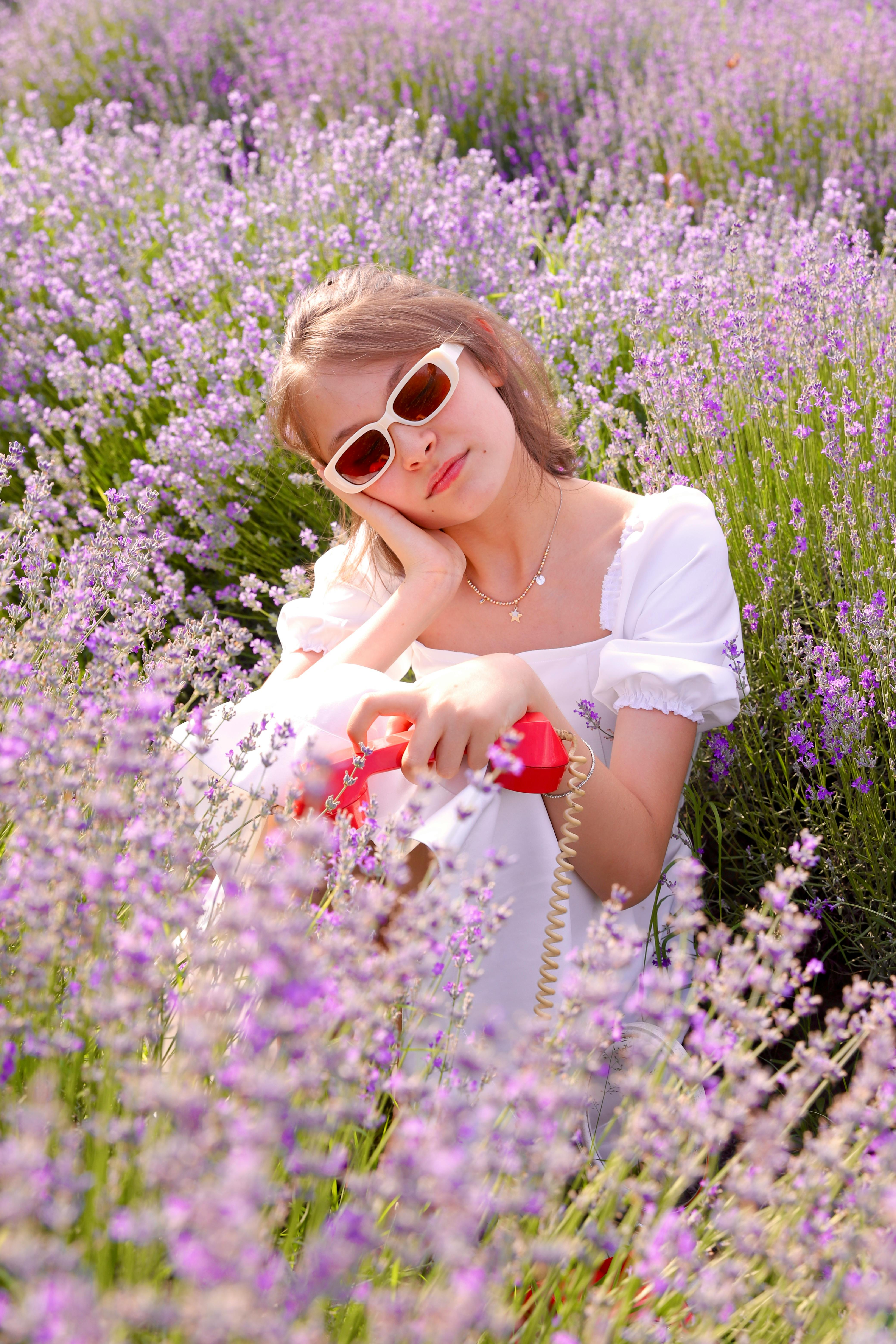 Woman in white dress among lavender flowers holding a red vintage handset.