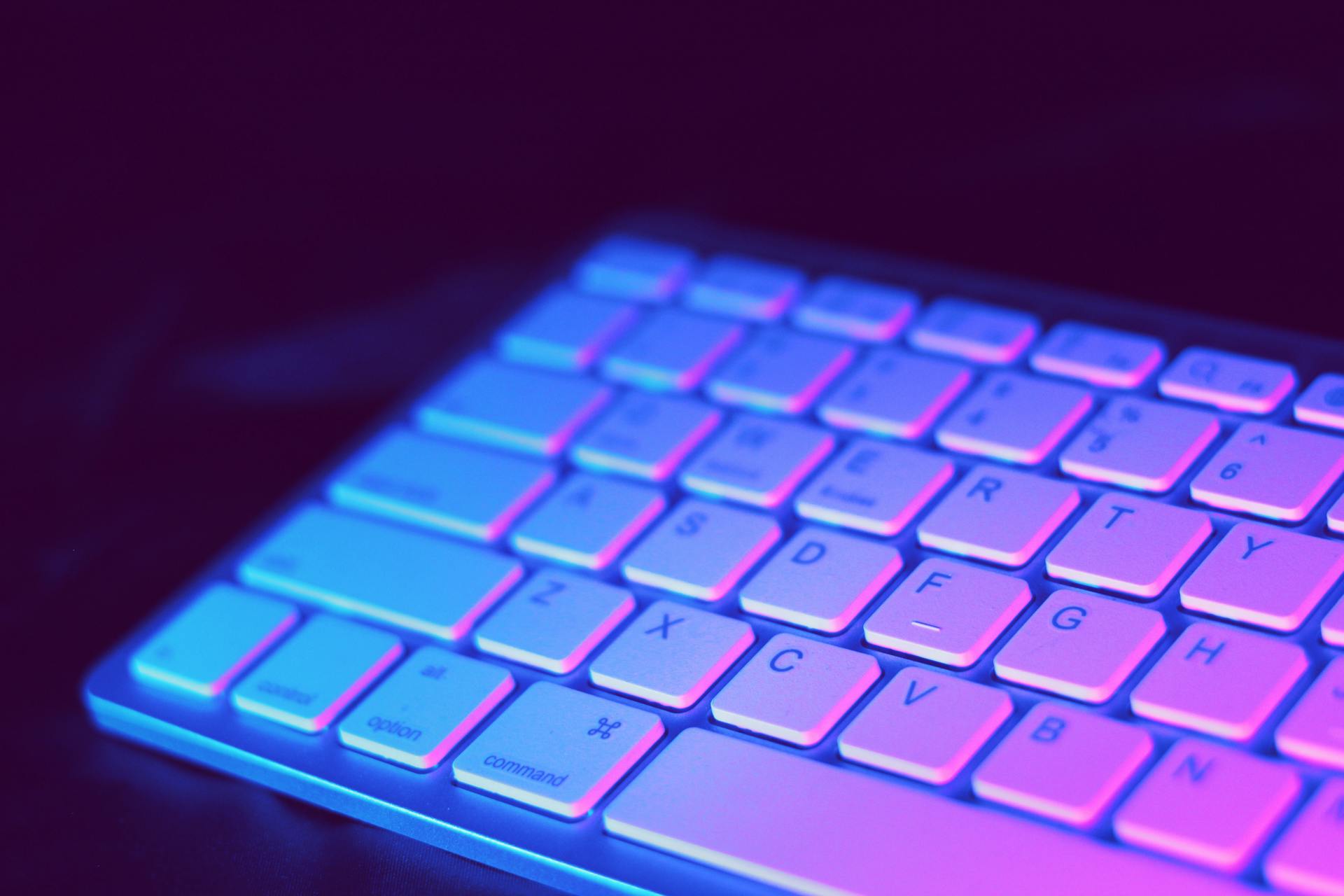 Close-up of a modern keyboard illuminated with vibrant purple and blue neon lighting.