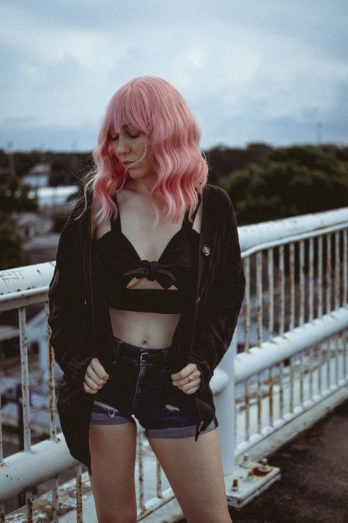 Free Stylish woman with pink hair in denim shorts and jacket on a city bridge. Stock Photo