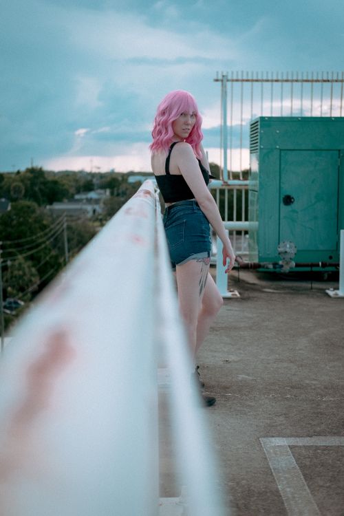 Free Fashionable woman with pink hair standing on an urban rooftop, showcasing a modern edgy look. Stock Photo