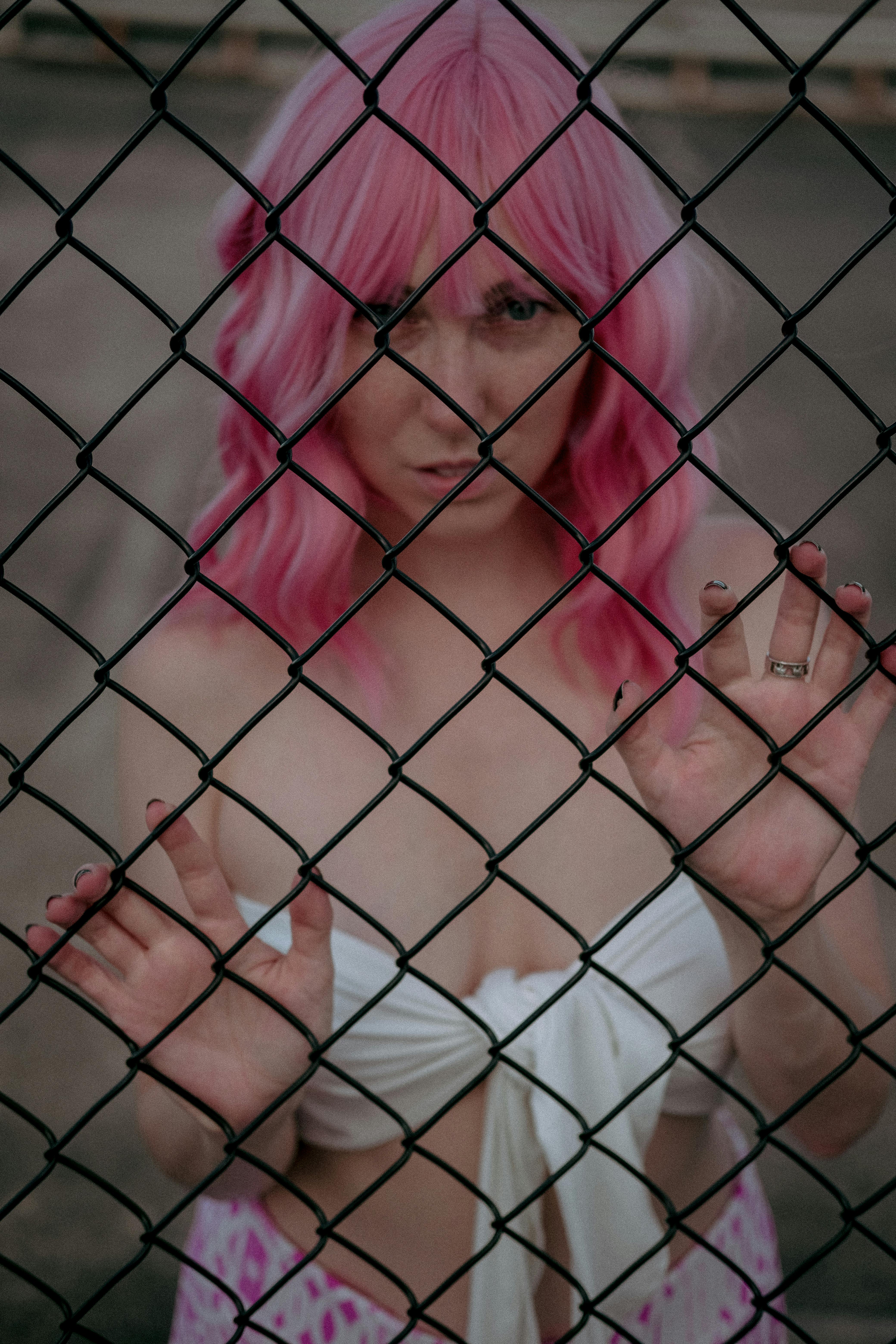 woman with pink hair holding on chain link fence
