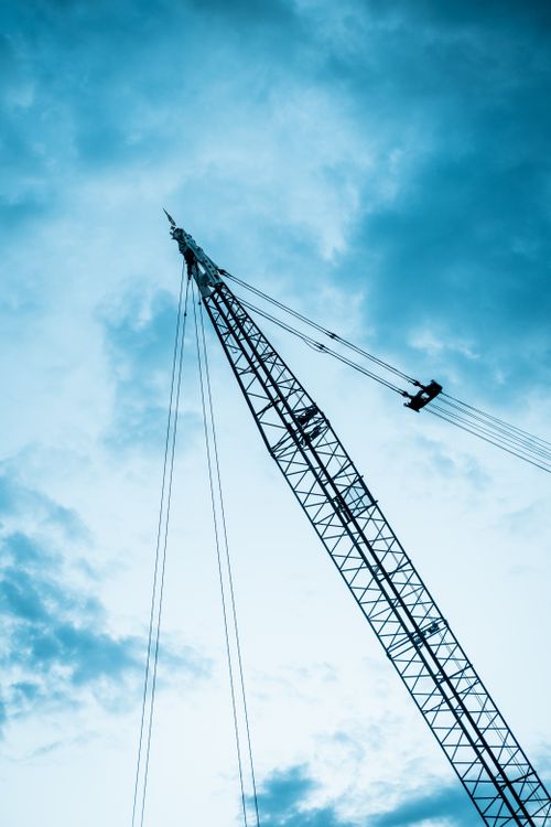 Free A dramatic view of a construction crane silhouetted against a cloudy sky at day. Stock Photo