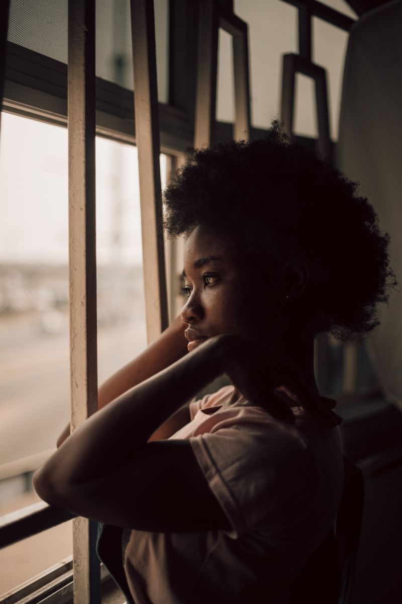 A Black woman looks out a window in a quiet, reflective moment. Depression in Black women is real and treatable, and asking for help is a sign of strength.